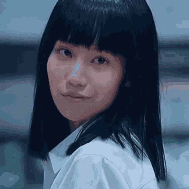 a girl with long black hair and bangs is wearing a white shirt and smiling .