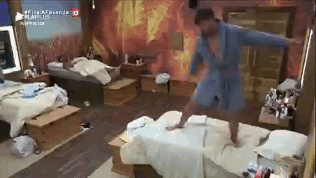 a man in a robe is standing on a bed in a messy room .