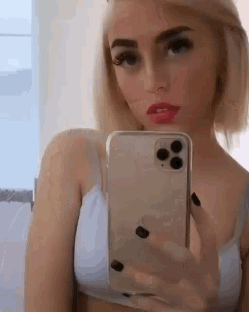 a woman is taking a selfie with her phone in a white bra .