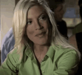 a woman in a green shirt is sitting at a table and smiling .
