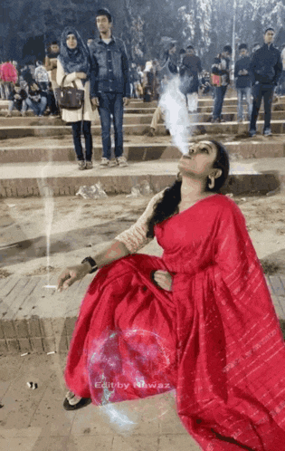 a woman in a red saree is smoking a cigarette in a crowded area