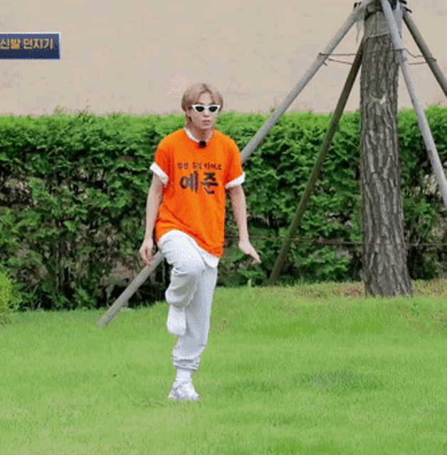 a man wearing an orange t-shirt with chinese writing on it is running in the grass