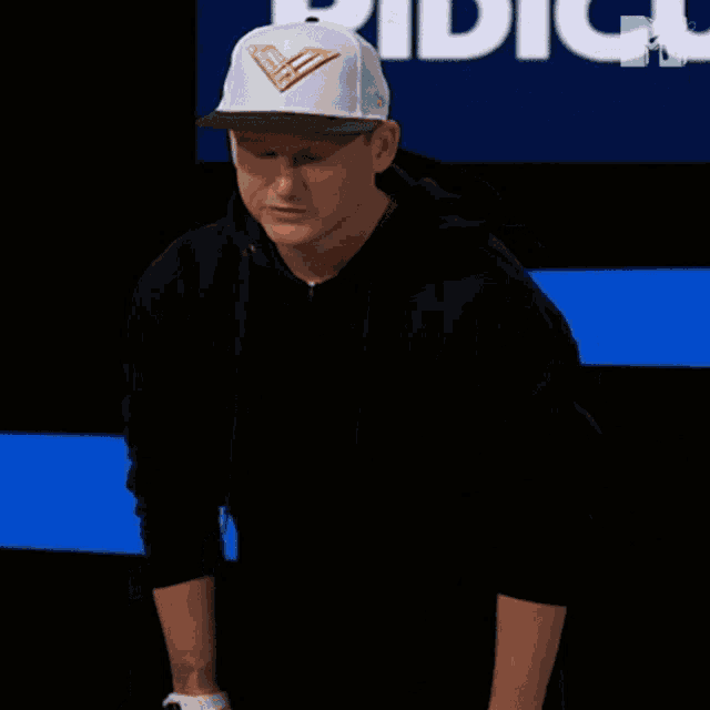 a man wearing a hat and a black hoodie is standing in front of a mtv logo