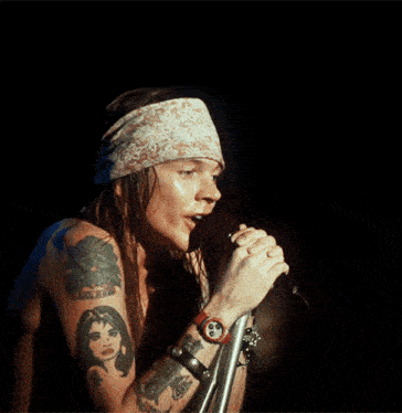 a shirtless man singing into a microphone wearing a headband