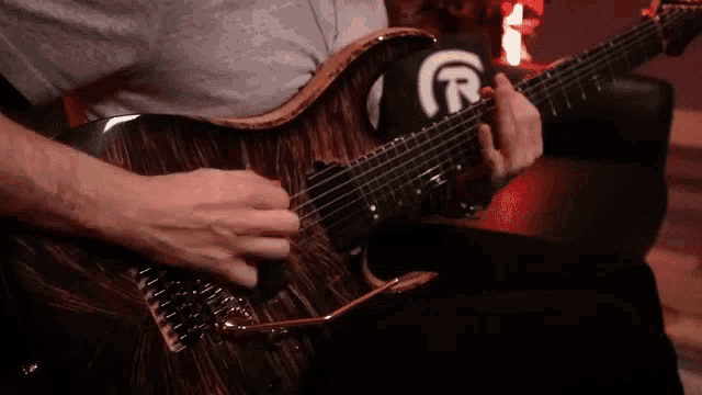 a man is playing a guitar with a r on the back of his shirt