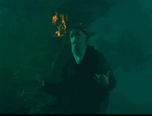 a man with a mask on his face stands in a dark forest