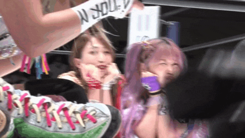 a group of women are sitting in a stadium watching a wrestling match . one of the women has purple hair .