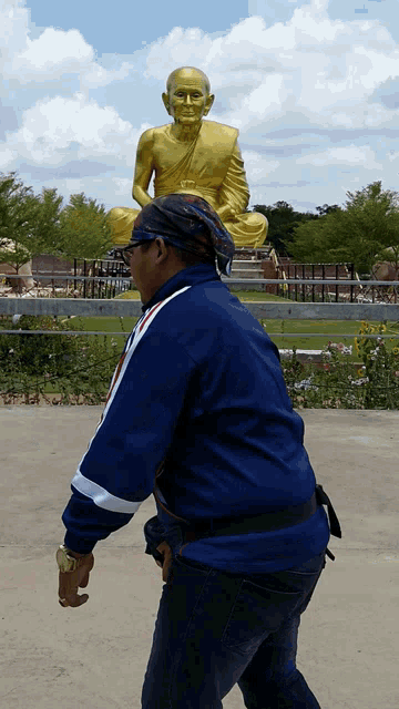 a man in a blue jacket is standing in front of a large gold statue