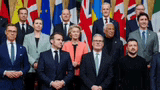 a group of people in suits and ties are standing in front of flags .