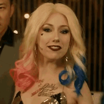 a woman is dressed as harley quinn from the movie suicide squad and has a tattoo on her chest .