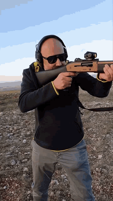 a man wearing headphones and sunglasses is holding a shotgun with a scope