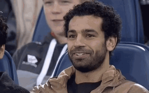 a man with a beard is smiling while sitting in a stadium seat .