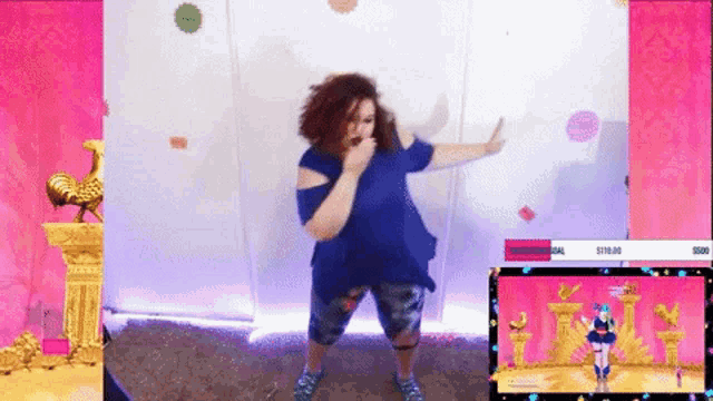 a woman in a blue shirt is dancing in front of a video game screen