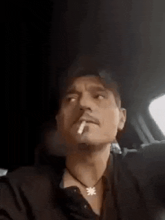 a man is smoking a cigarette in a car while wearing a necklace .