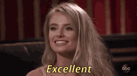 a woman is smiling and saying excellent while sitting in front of a red curtain .