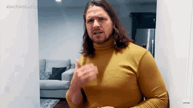 a man with long hair wearing a yellow turtleneck is standing in front of a wall that says #dalton 'scastle