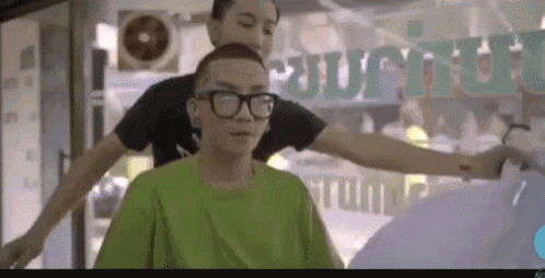 a man wearing glasses is getting his hair cut by a man wearing a green shirt