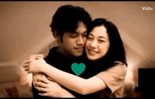 a man and a woman are hugging with a green heart in the middle of the hug