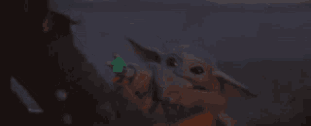 a baby yoda from star wars is holding a green object in his hand .