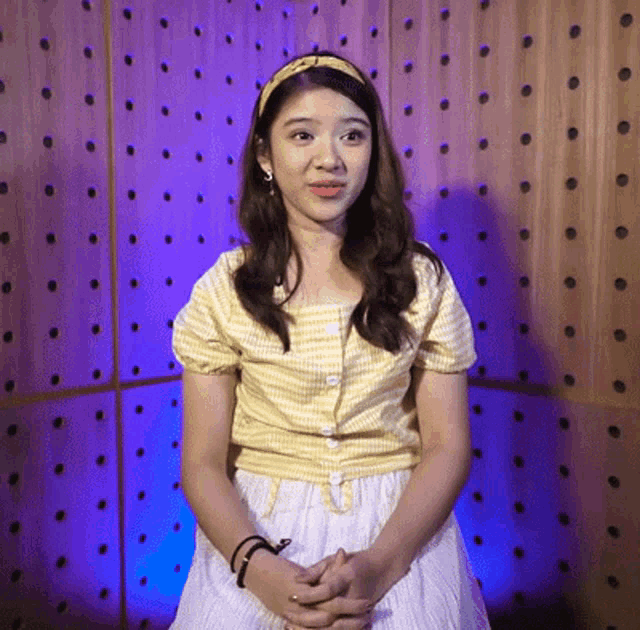 a woman wearing a yellow top and white skirt is sitting in front of a wooden wall with polka dots