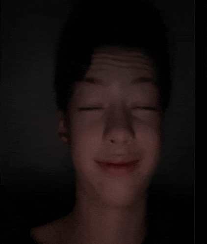 a young boy is making a funny face with his eyes closed in the dark .