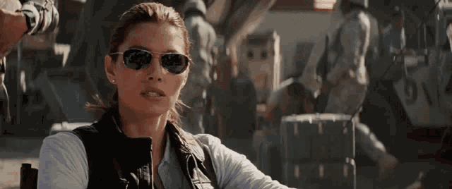 a woman wearing sunglasses is sitting in front of a group of men
