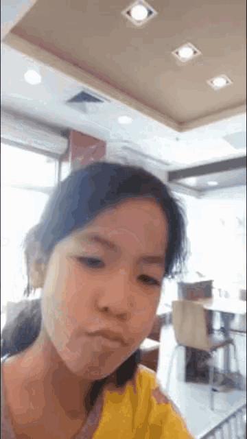 a little girl in a yellow shirt is making a funny face in a restaurant .