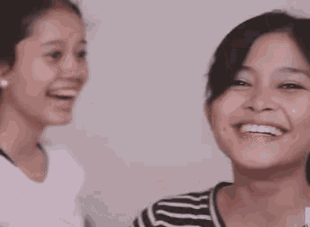 a woman in a striped shirt smiles while another woman holds her hand to her face
