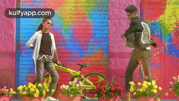 a man and a woman are standing next to a bicycle in front of a colorful wall .