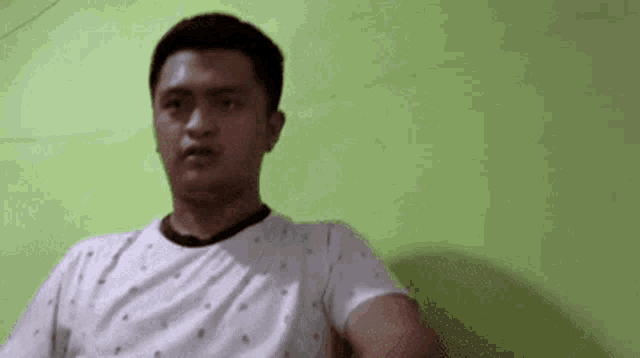 a man wearing a white shirt is sitting in front of a green wall .