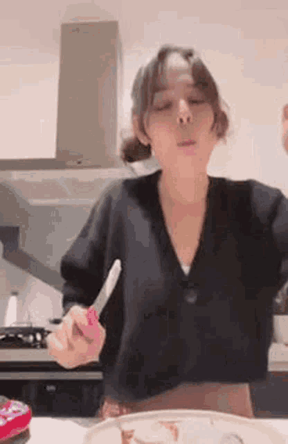 a woman in a black sweater is holding a knife in her hand in front of a plate of food .