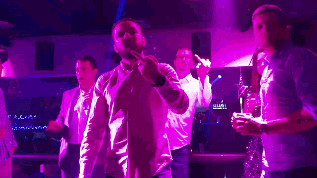 a group of people are dancing in a club with purple lights and a sign that says ' a & l ' on it
