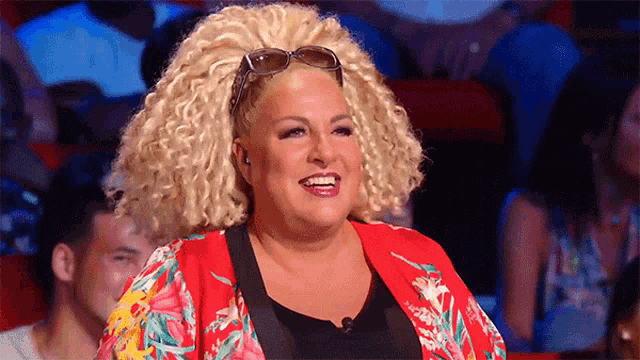 a woman with blonde curly hair wearing sunglasses and a red jacket is smiling .