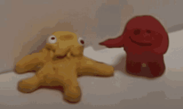 a yellow stuffed animal and a red stuffed animal are sitting next to each other on a white surface .