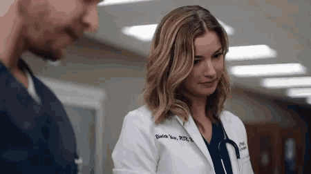 a woman in a white lab coat is standing next to a man in scrubs in a hospital .