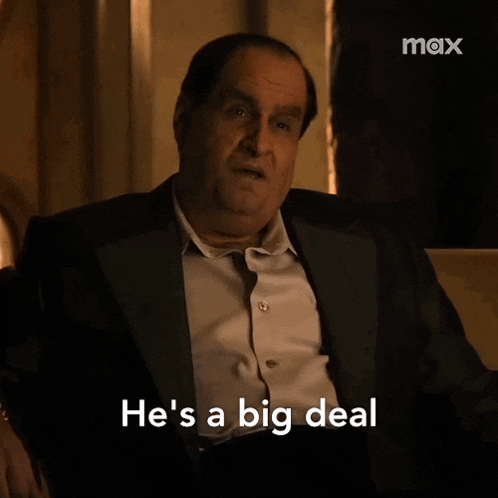 a man in a suit is sitting in a chair and saying he 's a big deal .