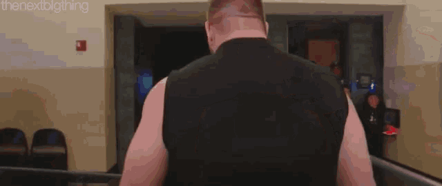 a man in a black tank top is walking down a hallway with the next big thing written on the bottom