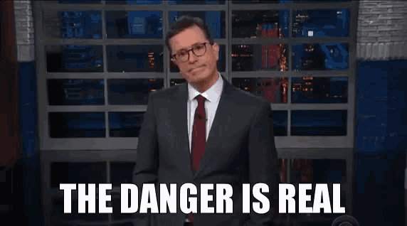 a man in a suit and tie is standing in front of a microphone and says the danger is real .