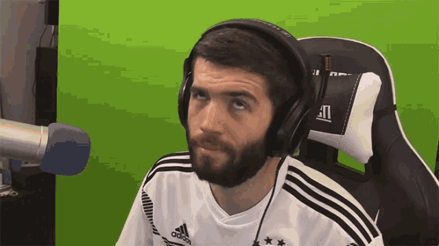 a man wearing headphones and an adidas shirt looks at the camera