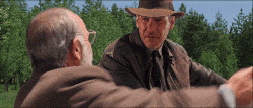 a man in a hat talks to another man in a field
