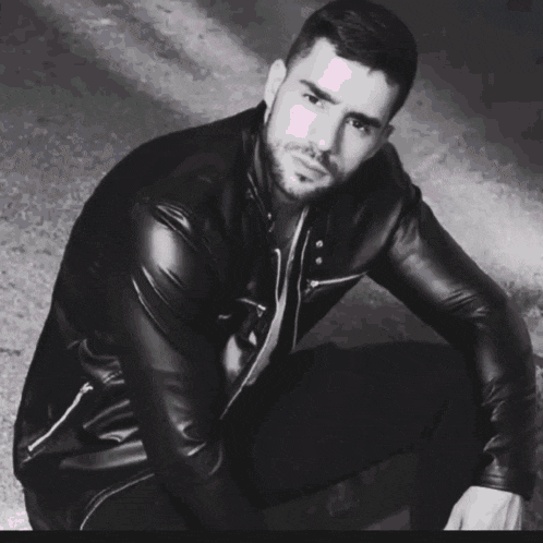 a man in a black leather jacket is kneeling down with the word gee behind him