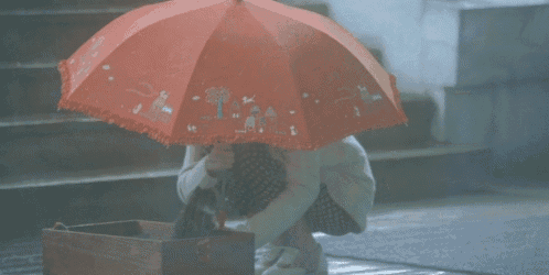 a person holding a red umbrella that has a tree on it