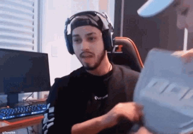 a man wearing headphones is sitting in front of a computer and holding a piece of paper .