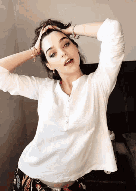 a woman in a white shirt has her hands on her hair