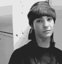 a black and white photo of a young man wearing a beanie and a piercing in his lip .