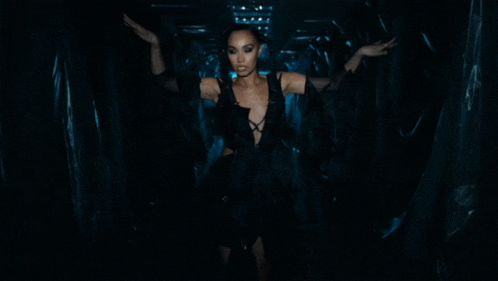 a woman in a black dress stands in a dark room
