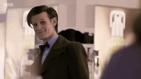 a man in a suit and bow tie is smiling and looking at another man in a room .