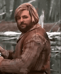 a man with a beard and long hair is standing in the woods