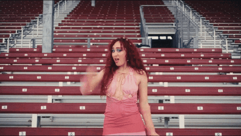 a woman in a pink dress is standing in a stadium with rows of red seats with the numbers 5 6 and 7
