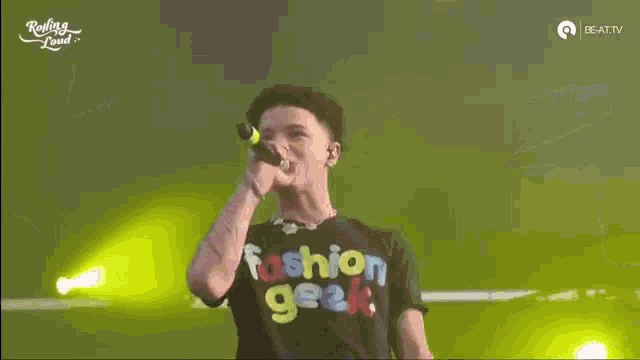 a young man is singing into a microphone on a stage in front of a crowd .